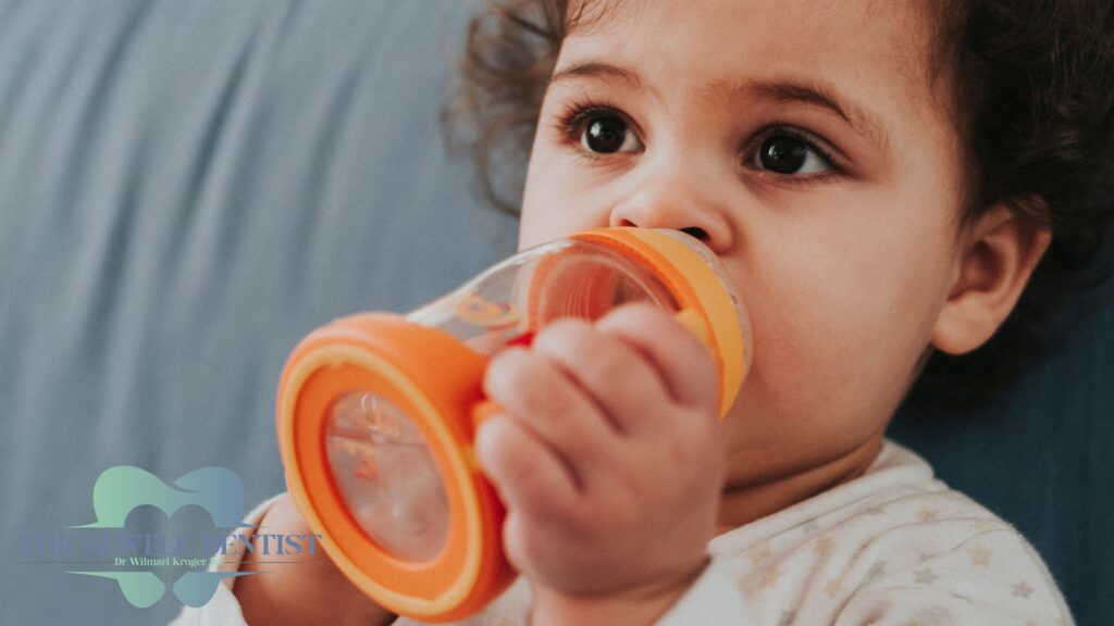 Baby Teeth Questions: Whatโs Normal, Whatโs Not, and What to Do About It 3 Toddler drinking from orange bottle, highlighting bottle feeding and early dental care.