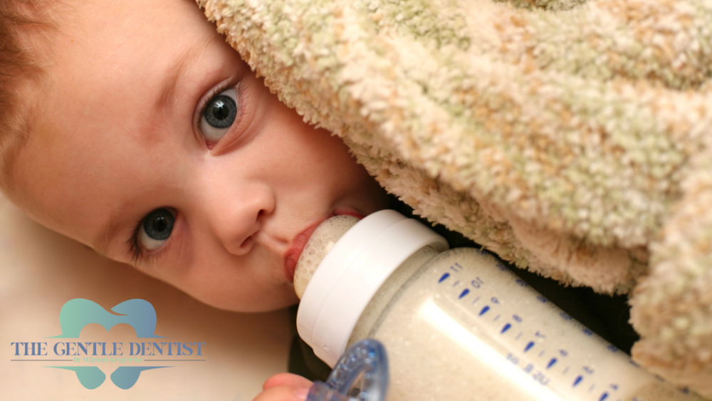 Bottle Mouth Syndrome Header Baby drinking from a bottle under a blanket, illustrating prolonged bottle use linked to bottle mouth syndrome.