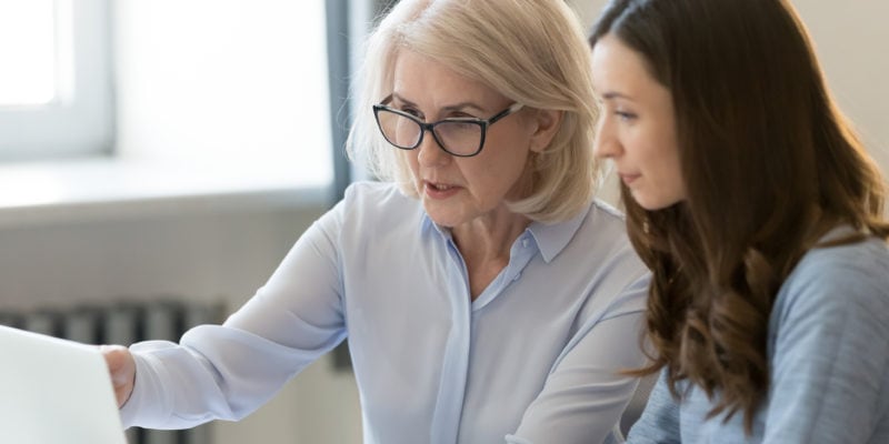 Two women discussing outreach strategies at a desk in an office setting.