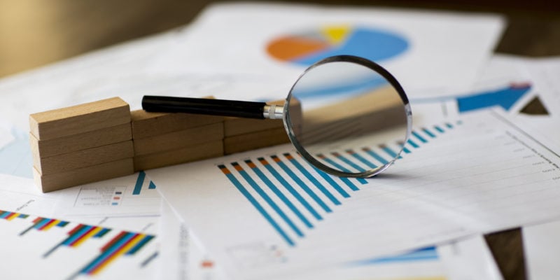Business analysis with magnifying glass over sales charts and reports.