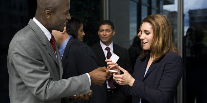 Business professionals exchanging contact information outside office building.