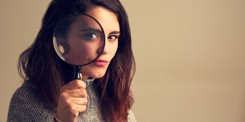 Woman holding magnifying glass, analyzing sales and marketing data.