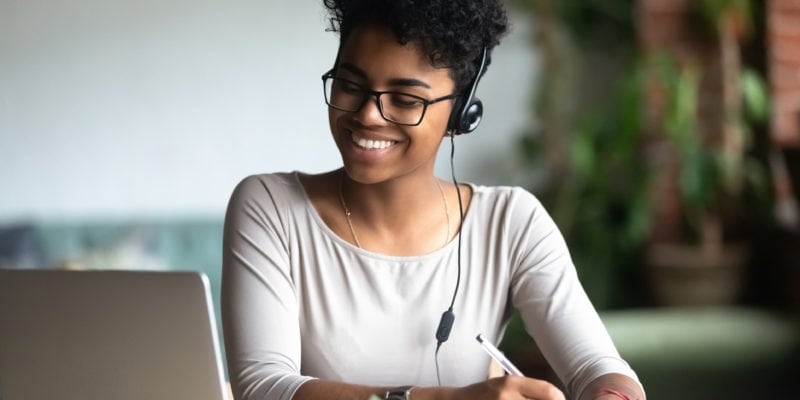 Customer service agent wearing headset, smiling while working at her desk for outbound calling.