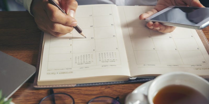 Person planning virtual appointment with a smartphone and calendar during COVID-19.
