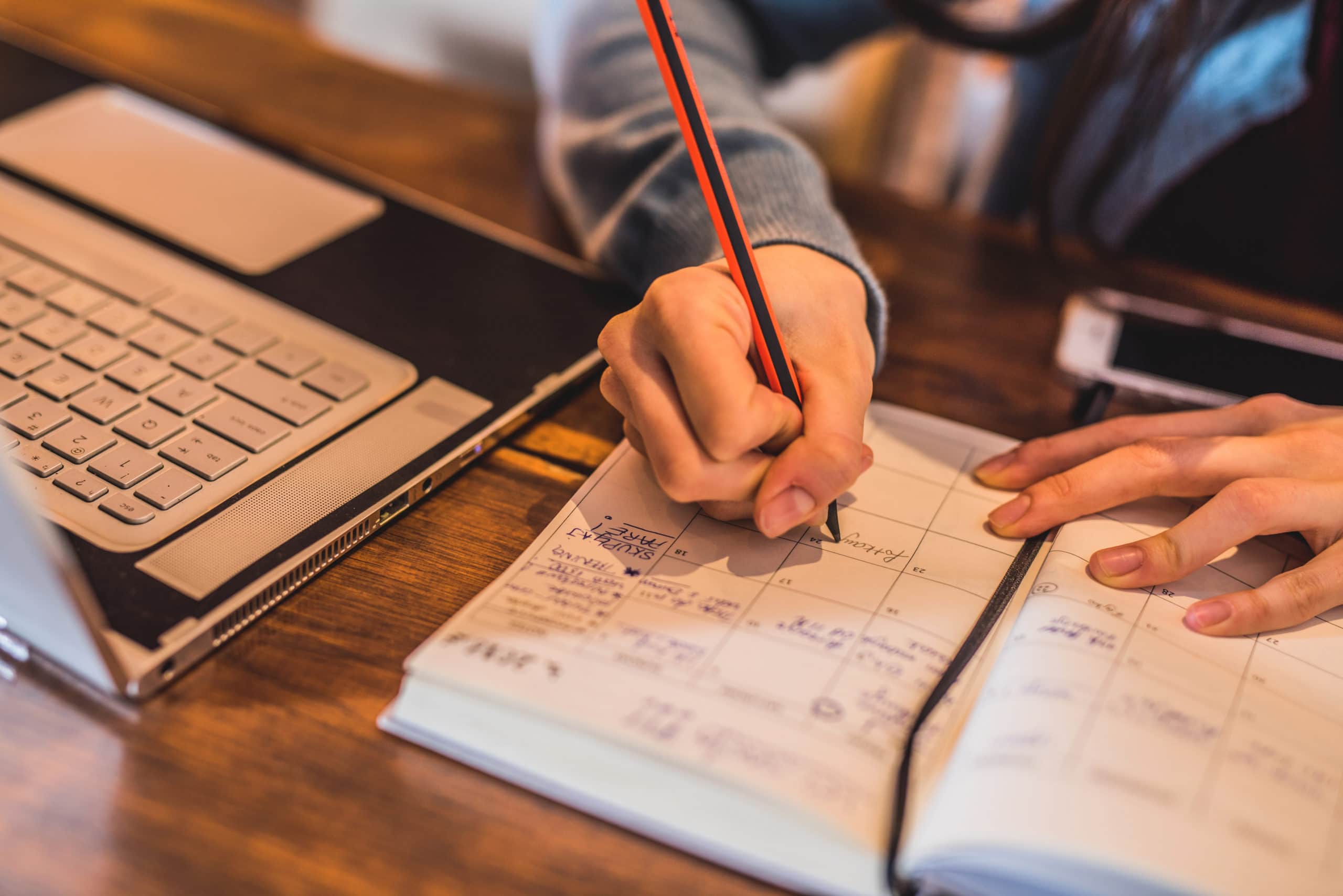 Market Research Planning Person writing in planner with laptop, planning appointment-setting campaigns.