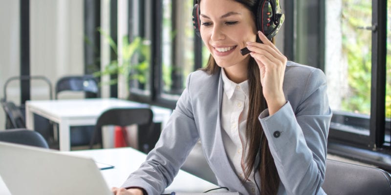 Customer support agent wearing a headset, working on a laptop in a modern office setting.
