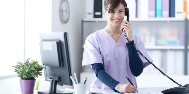 Woman in healthcare uniform making a phone call at her desk.