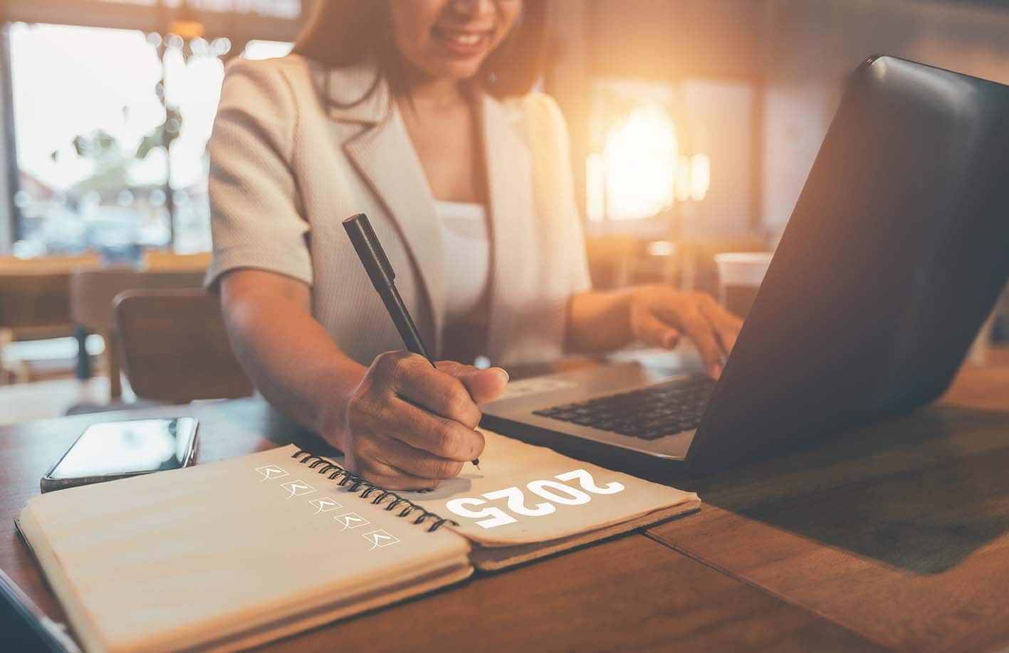 Lead Generation Strategies for 2025 Image of woman working at her laptop and writing 2025 on a notepad focusing on Lead generation trends 2025