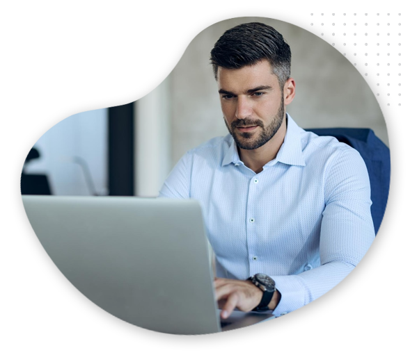 Blog-automation-img A man with short dark hair and a trimmed beard, wearing a light blue button-up shirt, sits at a desk and works on his laptop, focused on setting up Blog Automation.