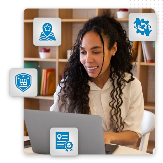 Build Local Trust feat img A person with long curly hair smiles while using a laptop at a desk, exploring Google My Business optimization. Four blue icons—a map pin, handshake, badge, and achievement—are overlaid, with bookshelves in the background.