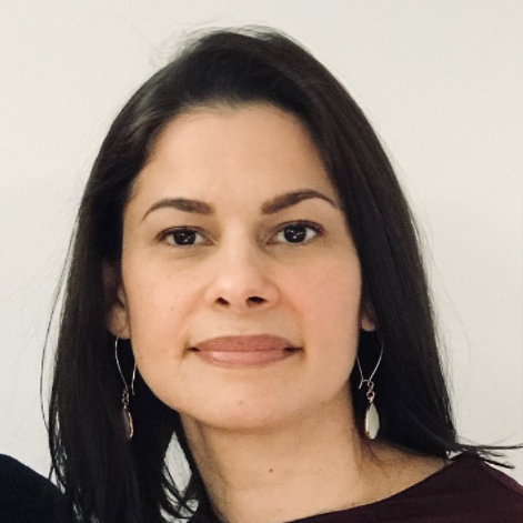 A woman with straight dark brown hair, wearing drop earrings and a maroon top, looks at the camera with a neutral expression against a plain light background—suggesting readiness for Enrollment in an Accelerator Program.