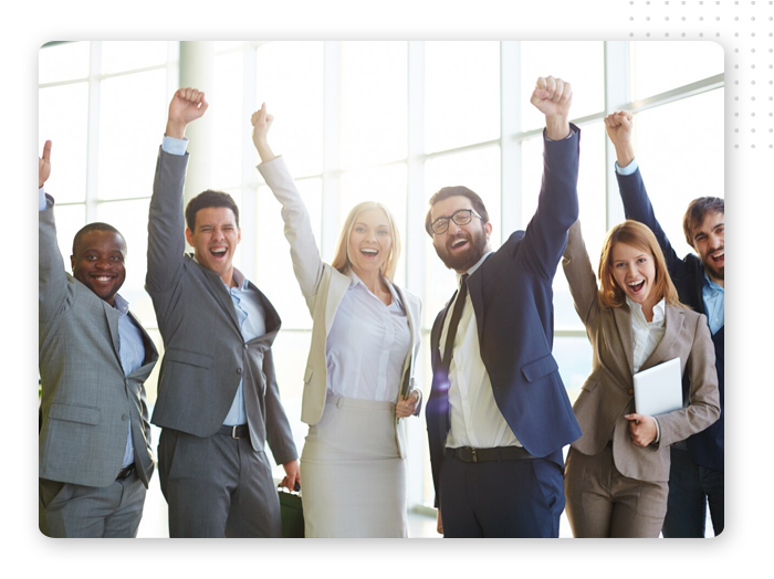 business-success-img A group of six business people in formal attire stand together indoors, smiling and raising their fists in celebration or excitement.