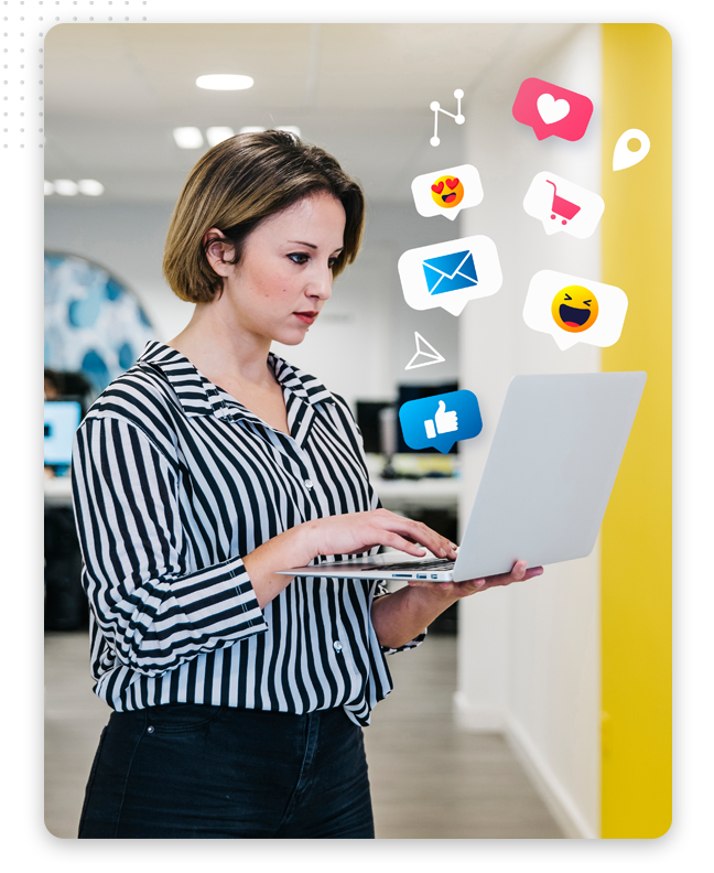 social-media-posting-process-feat-img A woman in a striped shirt stands indoors, using a laptop. Digital social media graphics—like thumbs up, heart, and message symbols—appear to float above her computer.