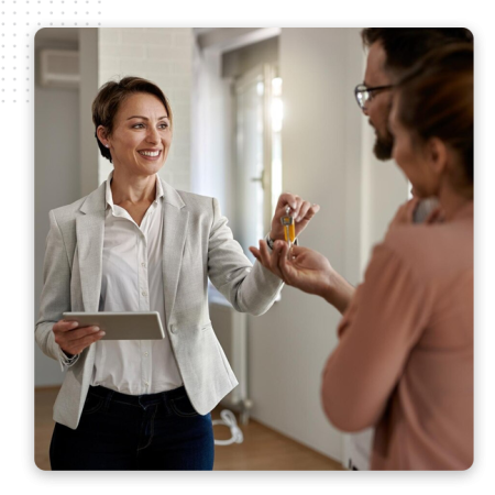 Automator-Professional-Agencies-Img A smiling real estate agent hands keys to a couple inside a bright, modern home, while holding a tablet and using an automation tool to streamline sales.