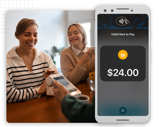 xtreme-automator-pos-integration-img Two women smile at a table as one pays with her smartphone using contactless payment; a mobile screen in the foreground displays a $24.00 purchase—effortless transactions powered by automation company innovations.
